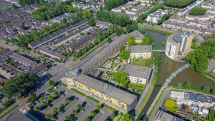 Luchtfoto van een woonwijk met verschillende woongebouwen, rijtjeshuizen, parkeerplaatsen, veel groen en water rondom de gebouwen